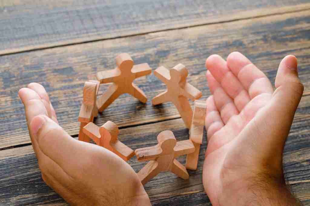 The 6 Primary Human Needs 3 business success concept wooden table top view hands protecting wooden figures people