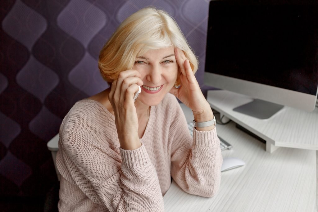 What Are The Effects of Stress On Mental Health? 2 smiling mature woman using mobile phone while working by computer home 1