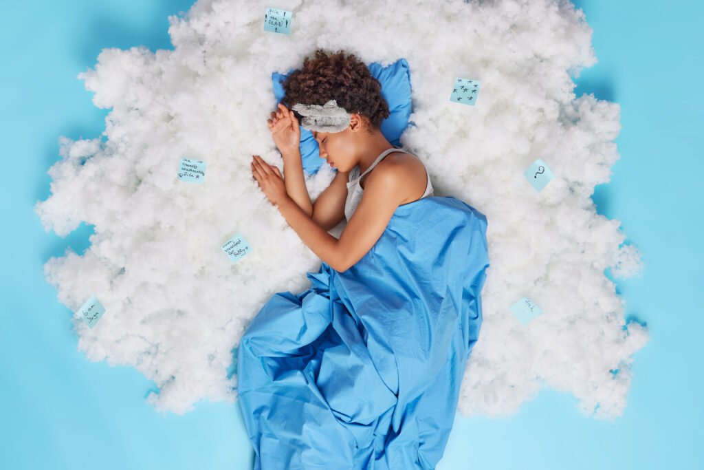 The Role of Dreams in Spiritual Awakening - Understanding Their Messages 2 Relaxed curly haired Afro American woman sleeps well has sweet dreams being stress free wears sleepmask covered with blanket uses stickers for making necessary notes lies asleep on white cloud