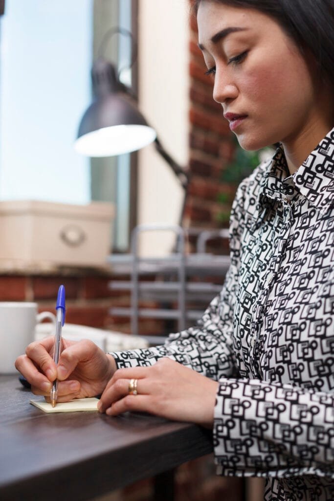 Using the 5x55 Method for Rapid Manifestation 4 Young productive asian businesswoman taking important notes while sitting at desk in company workspace. Marketing agency employee writing down client personal information regarding collaboration.