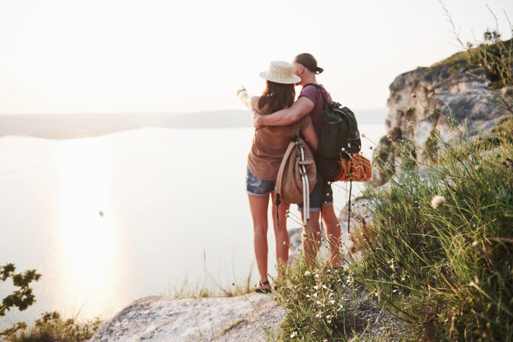 Manifesting Travel and Adventure - Using the Law of Attraction for Experiences 3 Two tourist male and woman with backpacks stand to the top of the crag and enjoying sunrise. Traveling mountains and coast, freedom and active lifestyle concept.