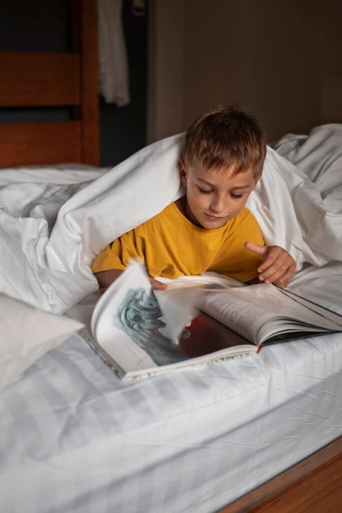 A boy reading a book before he goes to sleep